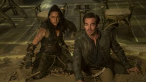 Barbarian Holga (Michelle Rodriguez) and bard Edgin (Chris Pine) kneel awkwardly in sand and shattered tiles in front of several chairs in Dungeons &amp; Dragons: Honor Among Thieves