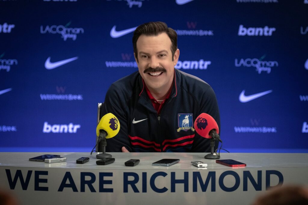 Ted Lasso sitting at a press conference in season 3