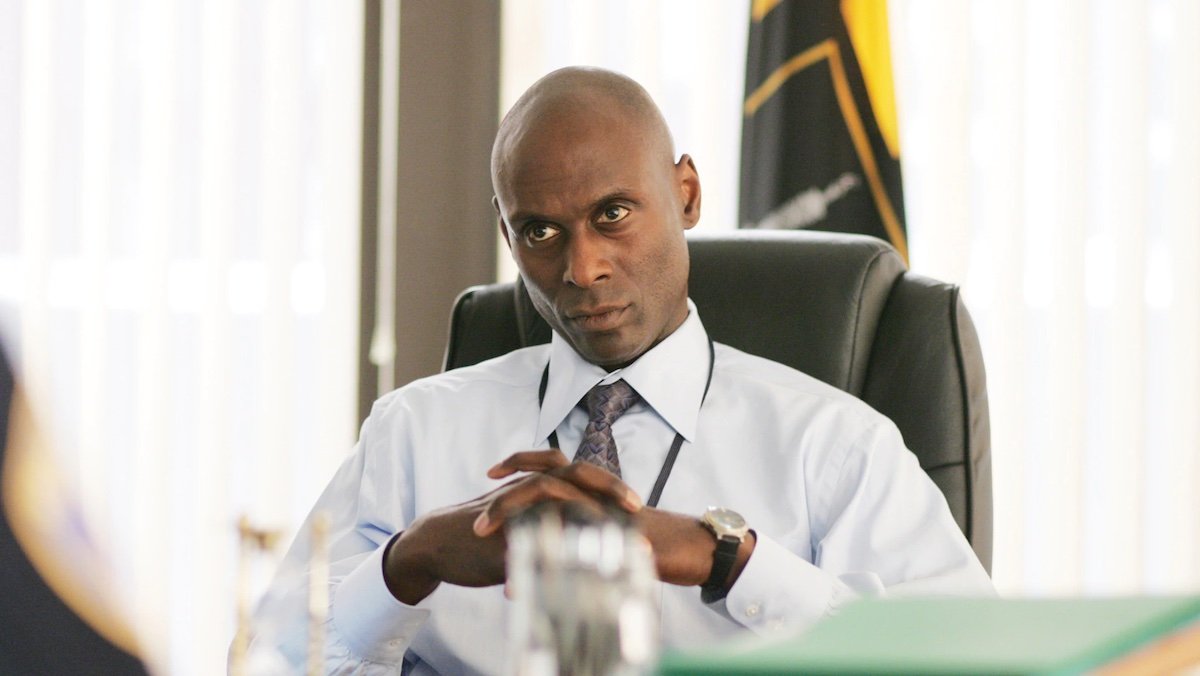 Lance Reddick as Cedric Daniels sits at his desk in a white dress shirt on The Wire