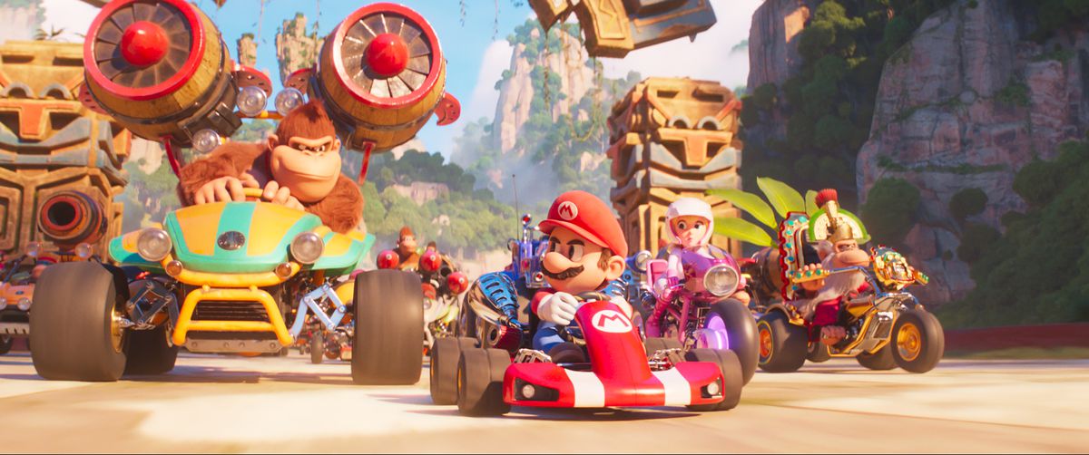 Mario drives his cart and looks back at Donkey Kong who is also driving his kart