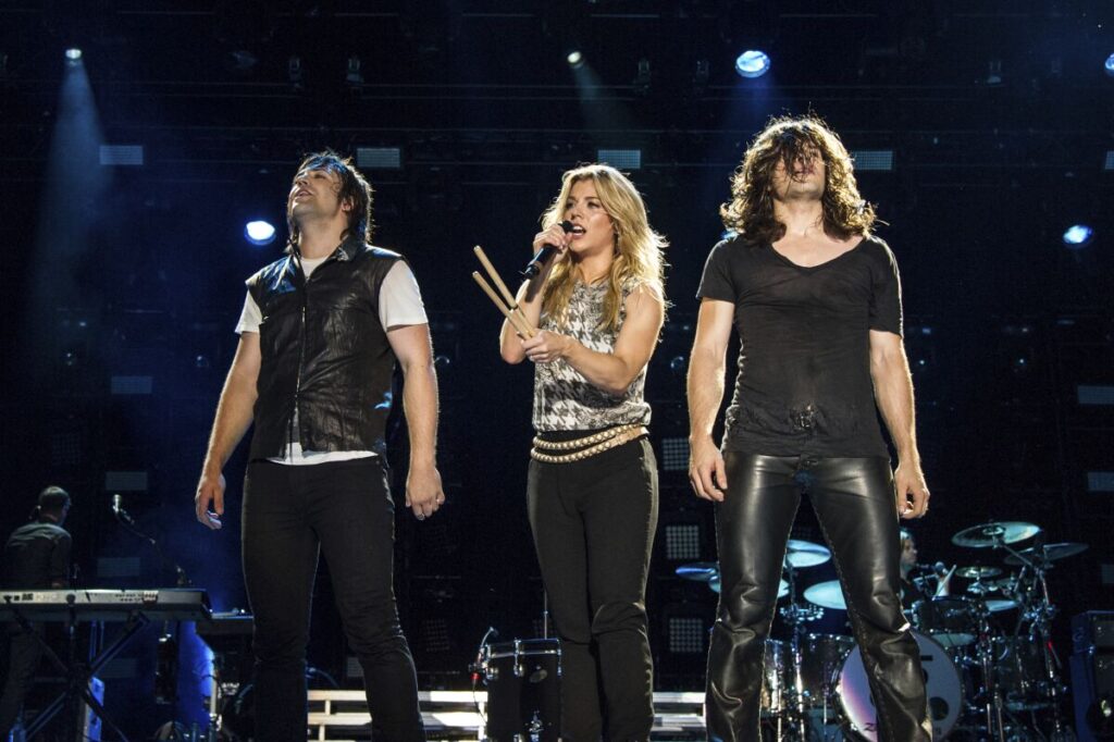 Neil Perry, Kimberly Perry and Reid Perry of The Band Perry wearing dark clothing standing on a stage