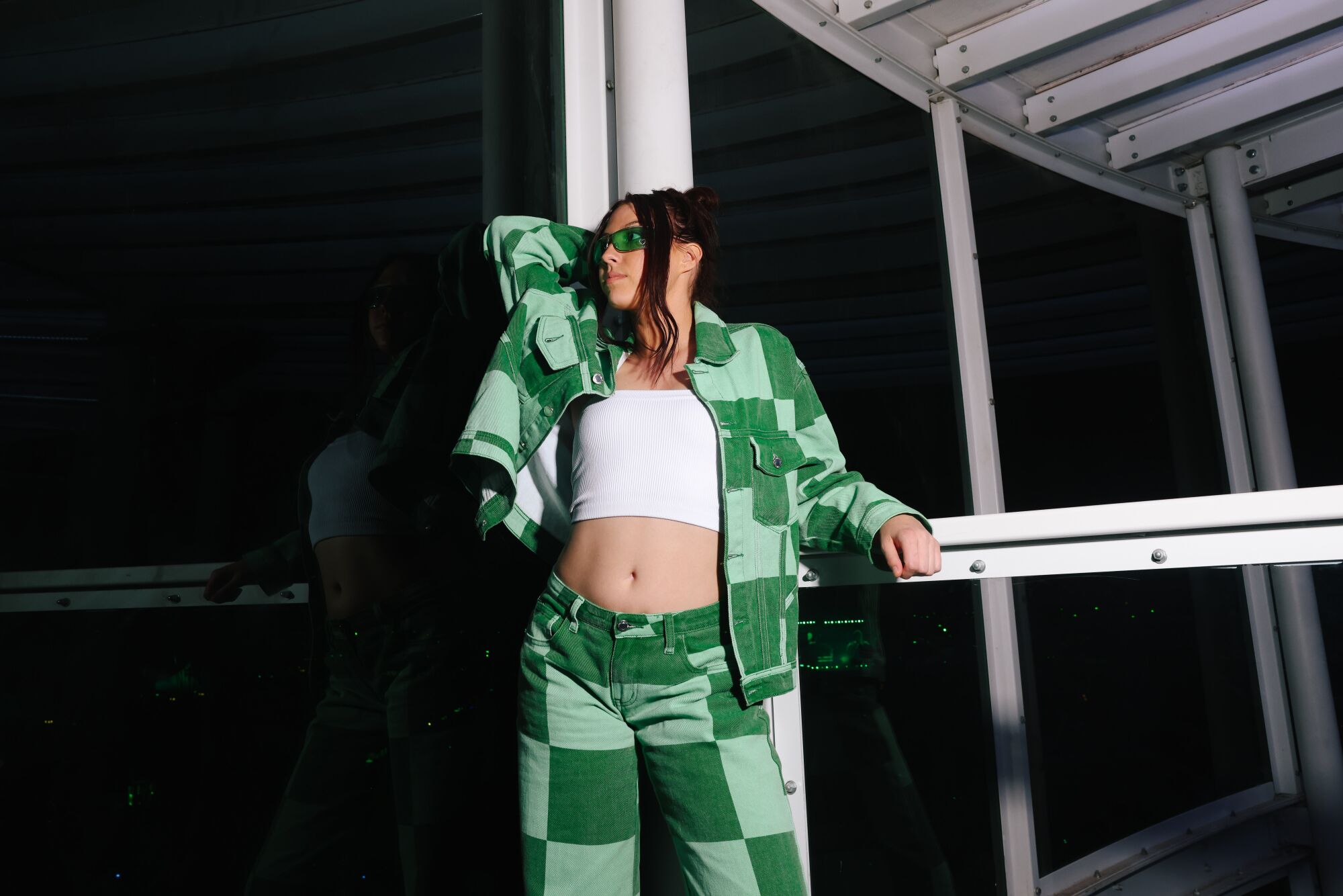 A woman in a green patterned jacket and pants poses with one elbow up near her face