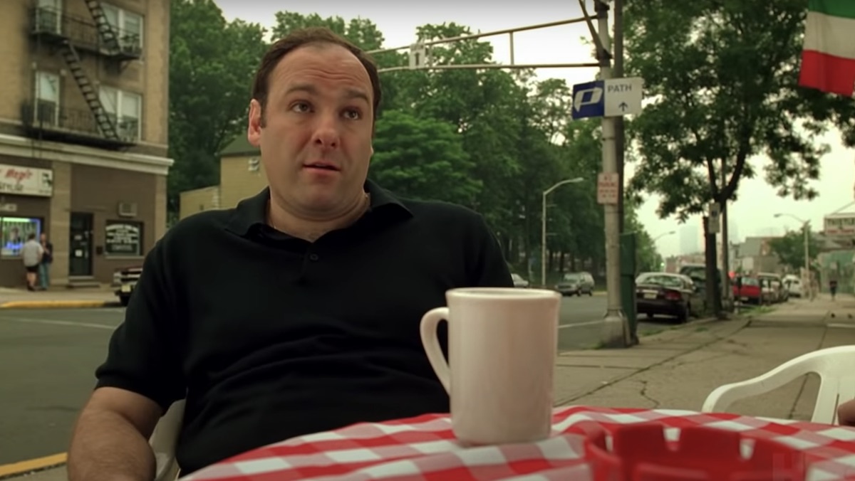 Tony Soprano sits at a table outside with a cup of coffee on The Sopranos