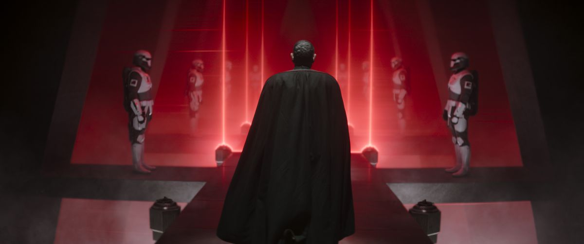 Moff Gideon stands before lasers and Dark Troopers lined up in a row in a scene from season 3 of The Mandalorian.