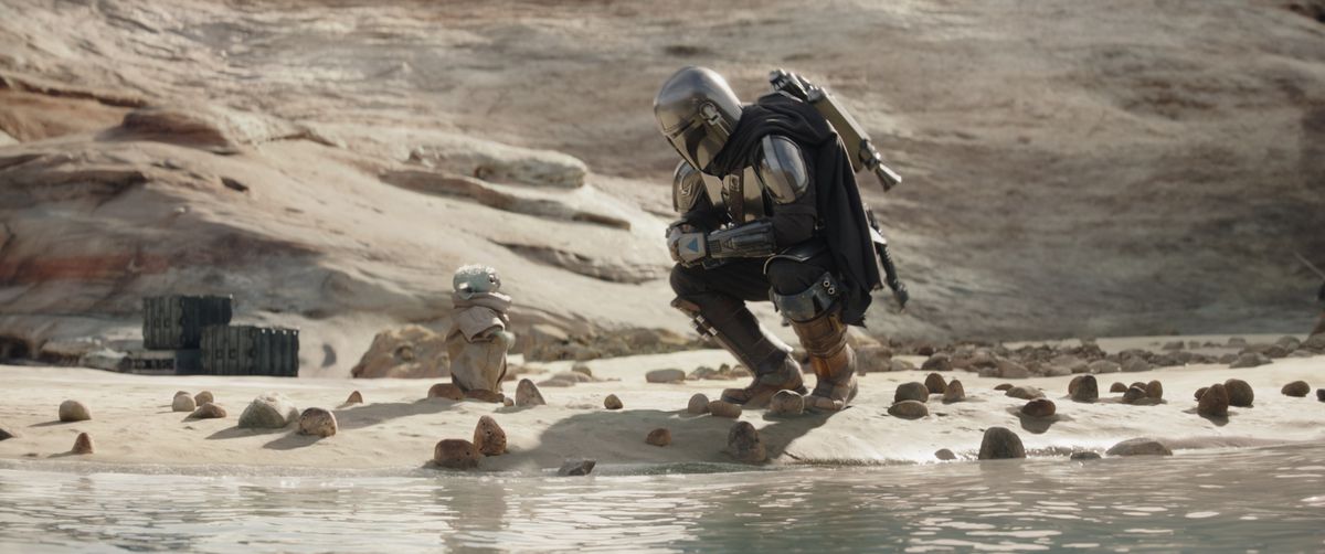 The Mandalorian crouches next to Grogu by some water in season 3 of The Mandalorian.