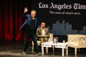 In a blue sportcoat and sneakers, Matthew Perry walks onstage toward a chair across from an interviewer