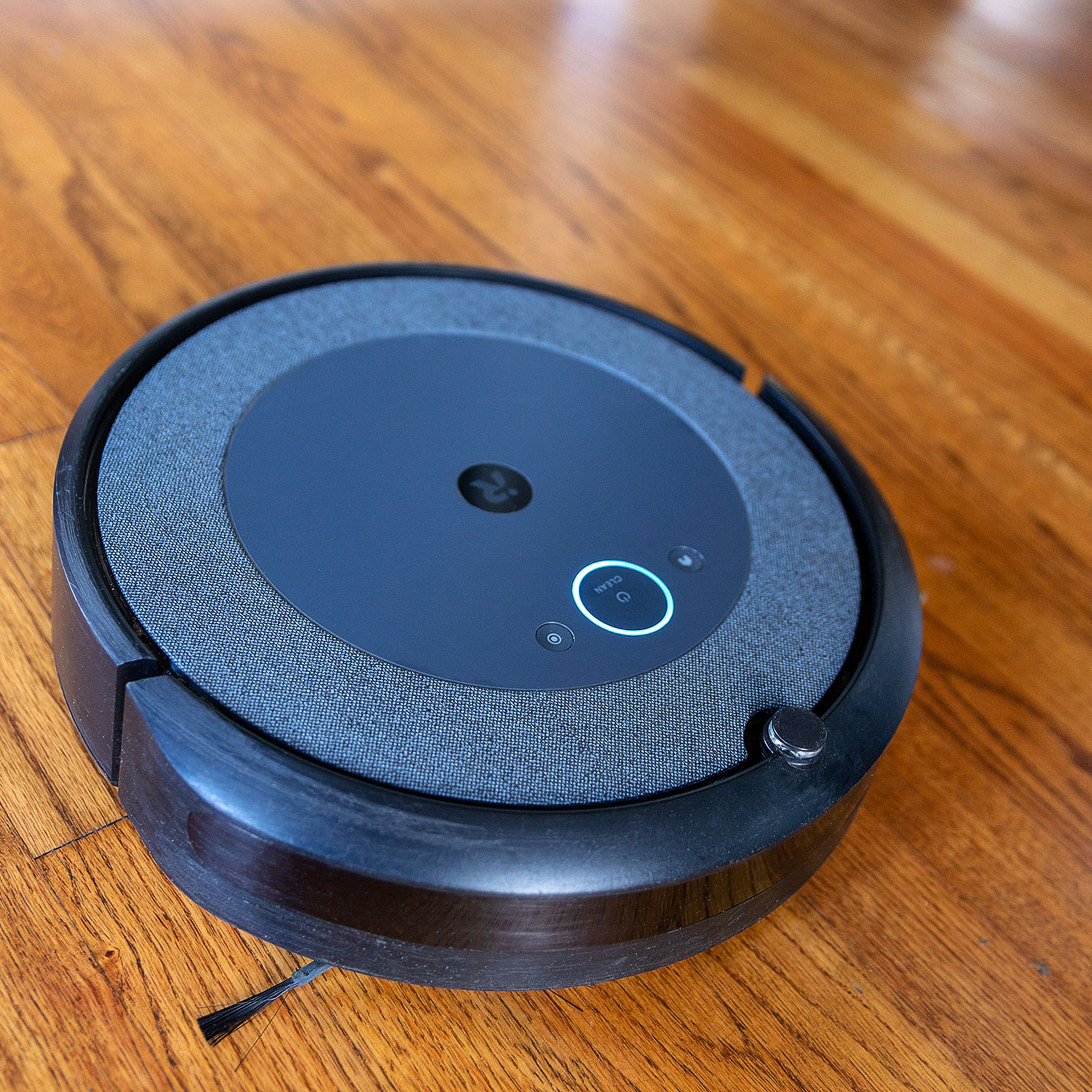 The iRobot Roomba i3 Plus EVO robot vacuum lying on a wooden floor.
