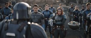 Bo-Katan and several of her Mandalorian associates stand in front of Paz Vizla with their helmets off (and Grogu) in season 3 of The Mandalorian.