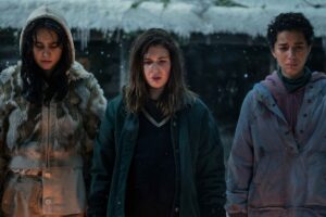 Lottie (Courtney Eaton), Shauna (Sophie Nélisse) and Tai (Jasmin Savoy Brown) standing and looking sad at something in a still from Yellowjackets season 2