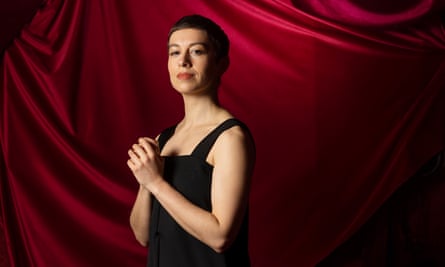 SuRie, who appeared in Eurovision 2018, standing in front of a red draped curtain 