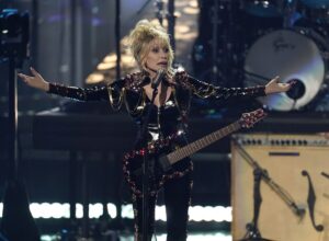 Dolly Parton onstage in a black jumpsuit with an electric guitar