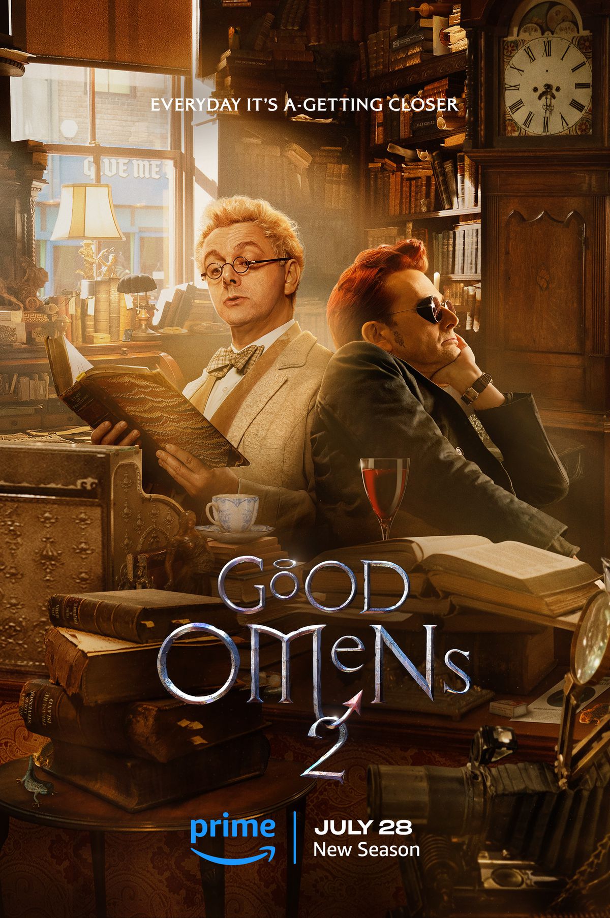 Michael Sheen as Aziraphale and David Tennant as Crowley, both lounging in a cluttered, golden-hued bookstore. 