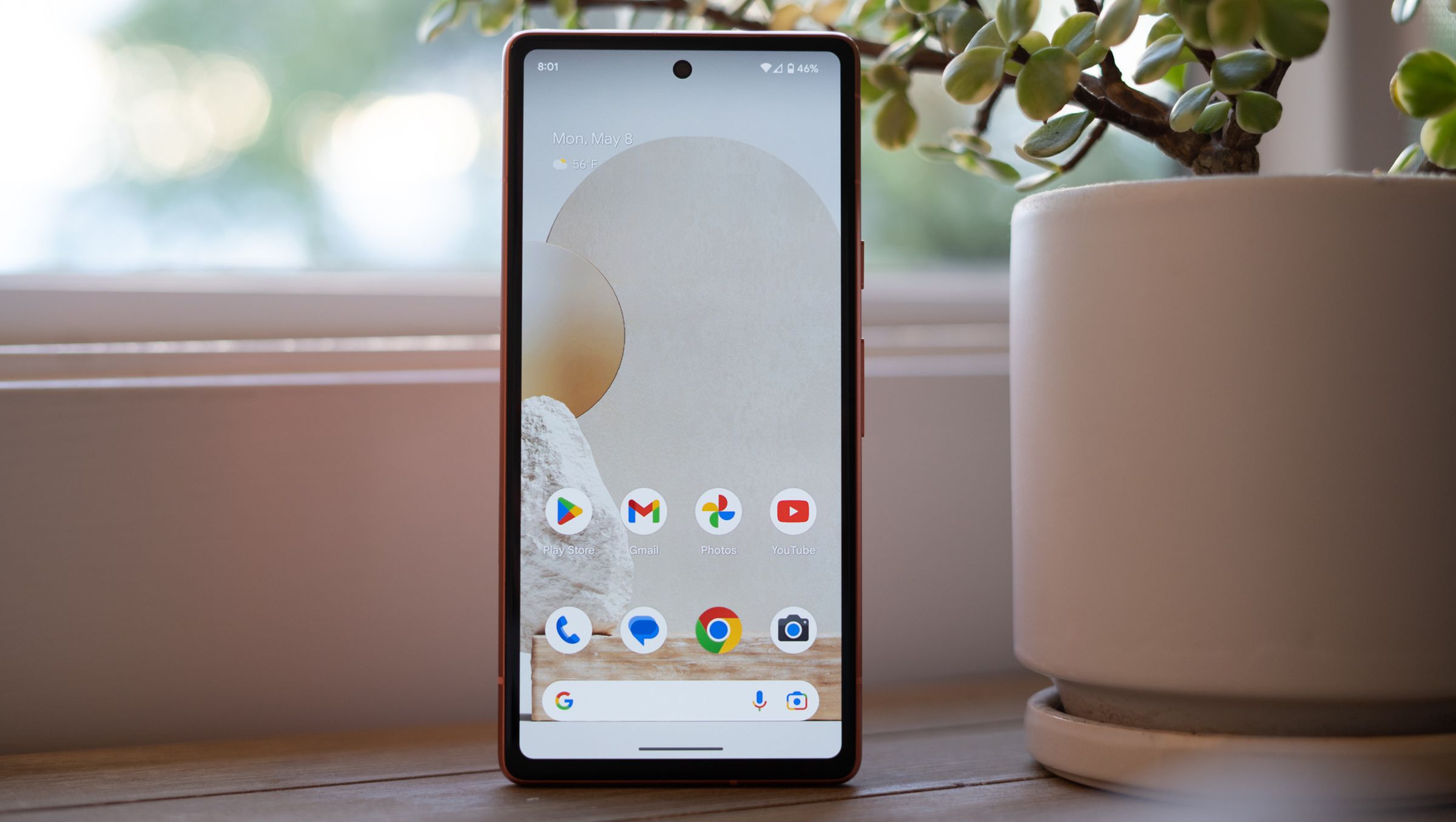 Google Pixel 7A standing upright on a table showing home screen.