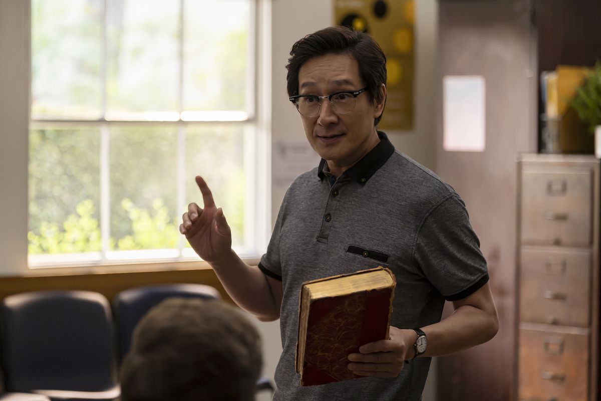 Ke Huy Quan in American Born Chinese. He’s holding a book in his hand and appears to be teaching in front of a class.
