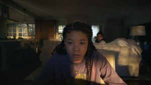 Storm Reid in Missing, looking at her computer screen in shock while her friend sits behind her on a couch