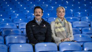 Ted and Rebecca sit alone in the stadium's blue chairs on Ted Lasso