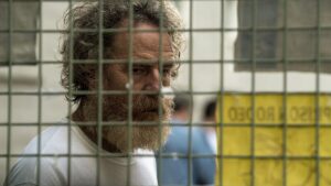 Bryan Cranston, long-haired and with a shaggy beard, is behind prison bars in a scene from "Your Honor."