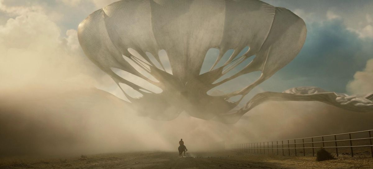 A large alien creatures floating in front of a man (Daniel Kaluuya) mounted on a horse with dust blowing in Nope.
