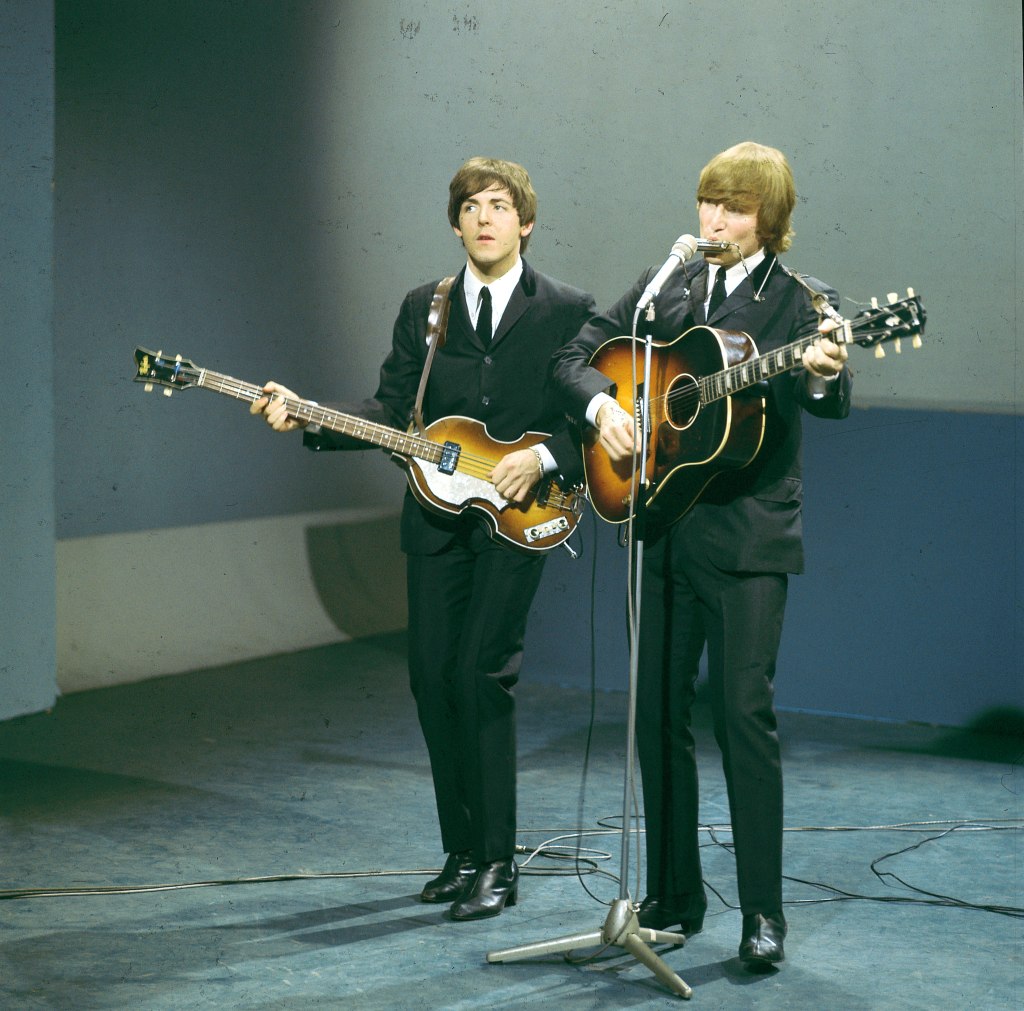 Paul McCartney (playing a Hofner 500/1 violin bass guitar) and John Lennon (playing a Gibson J-160E acoustic guitar) of English rock and pop group The Beatles perform on stage for the American Broadcasting Company (ABC) music television show 'Shindig!' at Granville Studios in Fulham, London on 3rd October 1964.