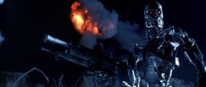 A T-800 Terminator exoskeleton surveying a battlefield with a battle rifle in hand as a fiery plume of smoke juts out in the distance in Terminator 2: Judgement Day.
