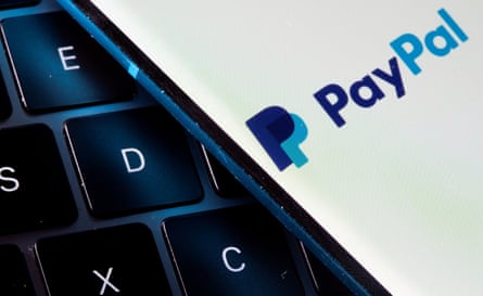 A smartphone with the PayPal logo is placed on a laptop