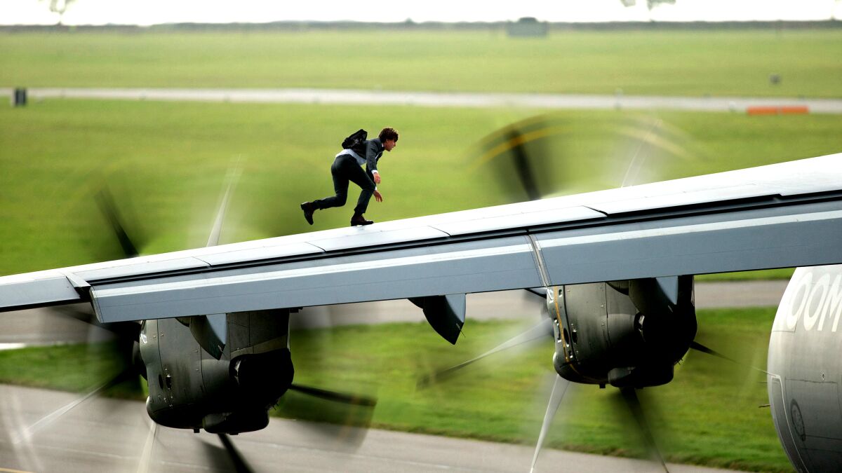 Tom Cruise walks on the wing of a plane as propellers spin.