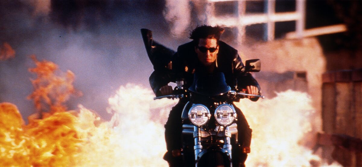 Tom Cruise rides a motorcycle away from a raging fire