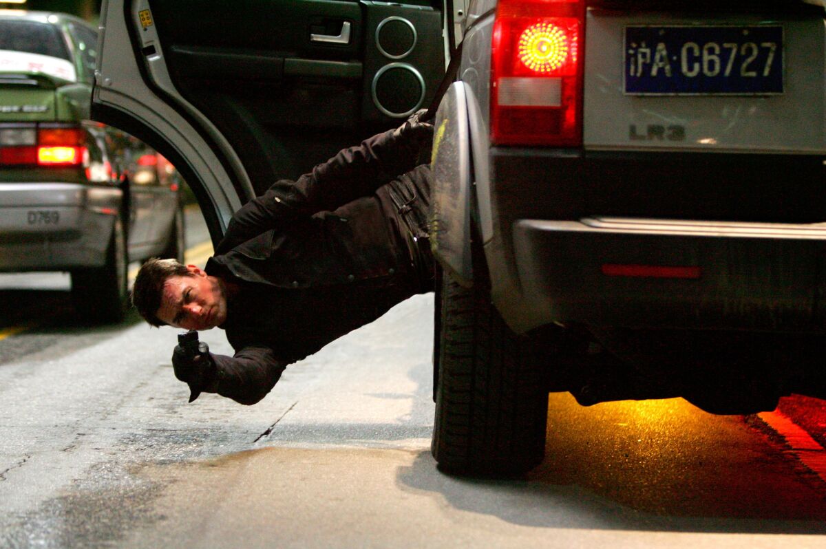 Tom Cruise brandishes a weapon while leaning out of a moving vehicle