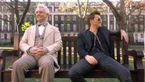 Michael Sheen and David Tennant smile on a park bench on Good Omens