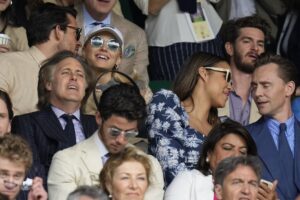 A group of celebrities and others watch a tennis match.