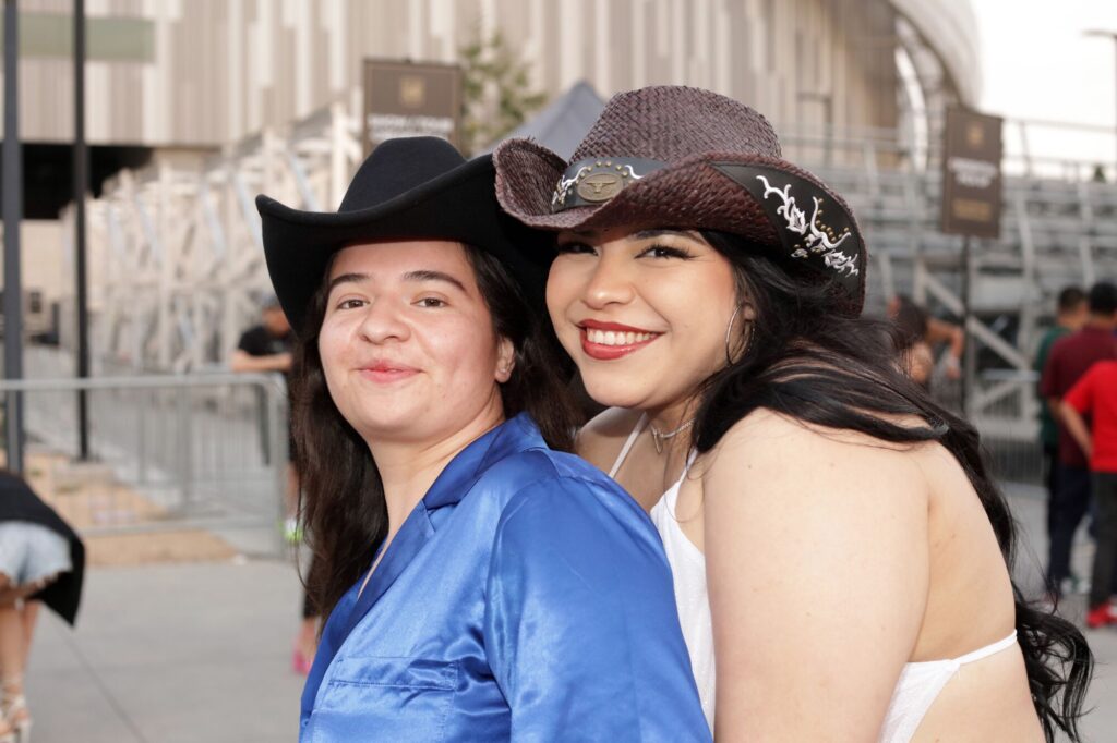 Smiling, cowboy hat-wearing Fuerza Regida fans at BMO Stadium.
