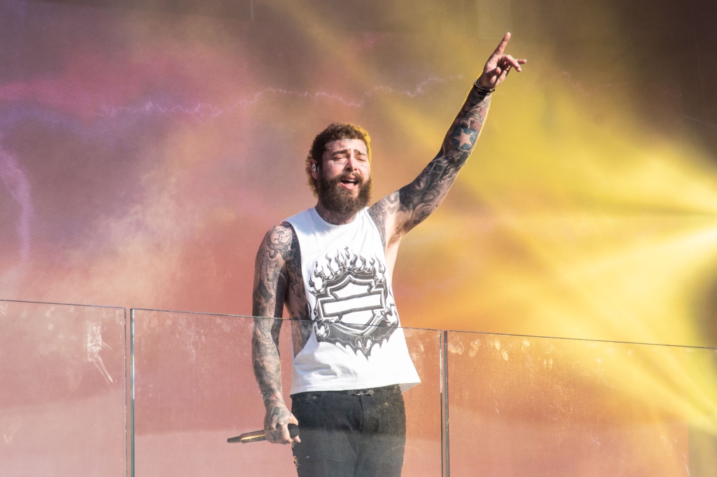 Malone raises a hand mid-performance, in a white tank top bearing a Harley-Davidson emblem.