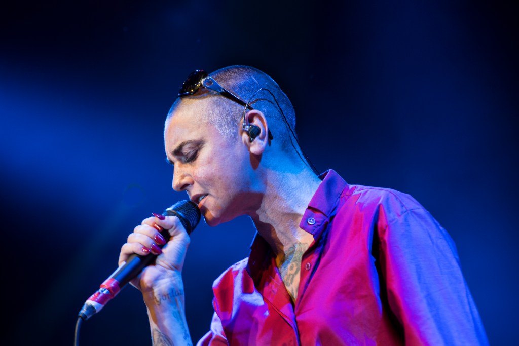 Irish singer-songwriter Sinead O'Connor singing on stage with microphone. 