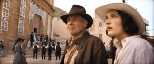 A still from Indiana Jones and the Dial of Destiny; Indy (at left) and new rival/partner Helena Shaw (right), both wearing fedoras, see something in the streets of Tangier.