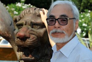 Japanese director Hayao Miyazaki stands next to a statue of a stylized lion with one hand on its head in Venice, Italy in 2008.