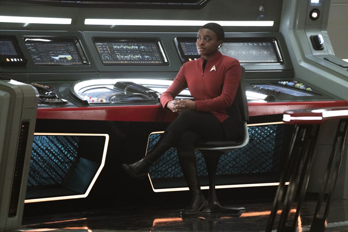 Uhura in a maroon and black uniform, sitting at spaceship controls.