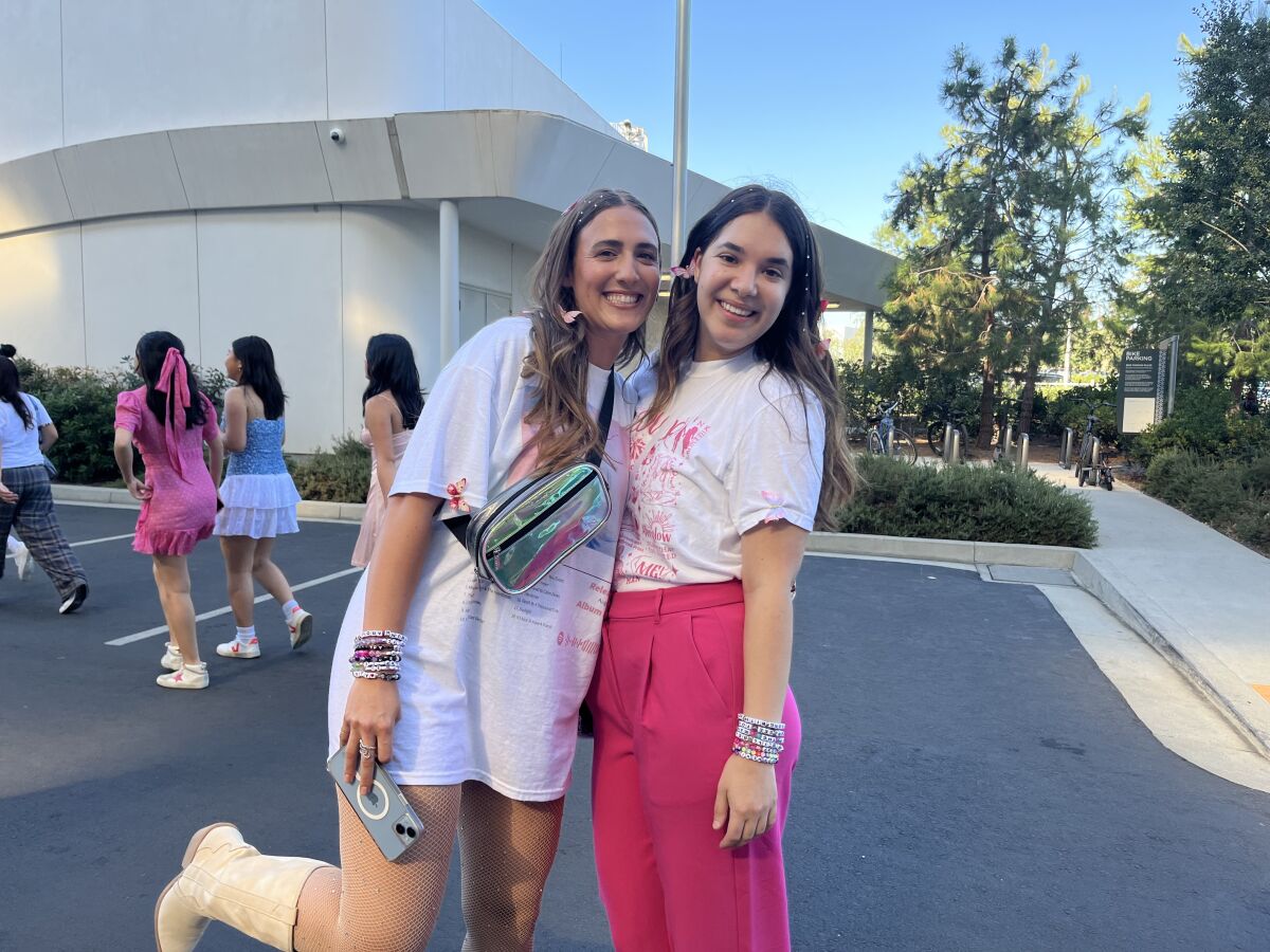 Two young women, one in cowboy boots, another in pink pants, smile as they pose outside a concert venue.