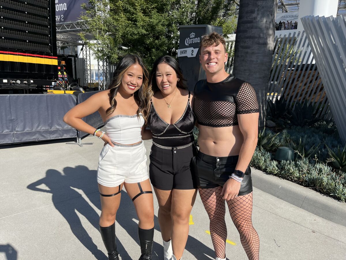 Three people, one in a white shorts outfit, one in a black shorts outfit and  another in mesh black top and fishnet hose.