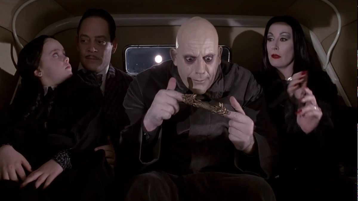 Wednesday Addams (Christina Ricci), Gomez Addams (Raul Julia), Uncle Fester (Christopher Lloyd), and Morticia Addams (Anjelica Huston) pile in the backseat of a car in The Addams Family (1991).