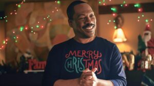 Eddie Murphy stands in front of christmas lights wearing a merry christmas shirt in candy cane lane trailer