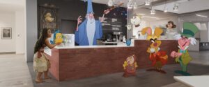 Animated Disney characters surround a receptionist’s desk at Disney Animation, including Merlin from The Sword in the Stone; Mrs. Potts, Chip, and Cogsworth from Beauty and the Beast; the Mad Hatter and March Hare from Alice in Wonderland, Moana from Moana, Flounder from The Little Mermaid, and more, in the Disney short Once Upon a Studio