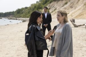 Kim Kardashian and Emma Roberts in AHS, standing on a beach together, while a bodyguard watches