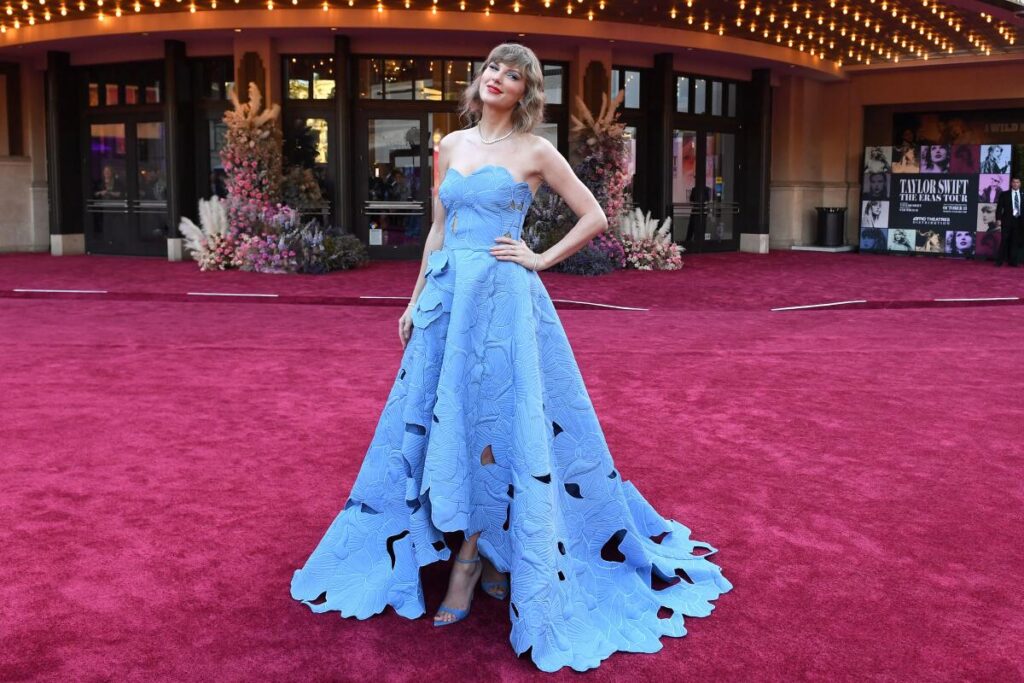 Taylor Swift posing on a red carpet in a blue dress with her hand on her hip