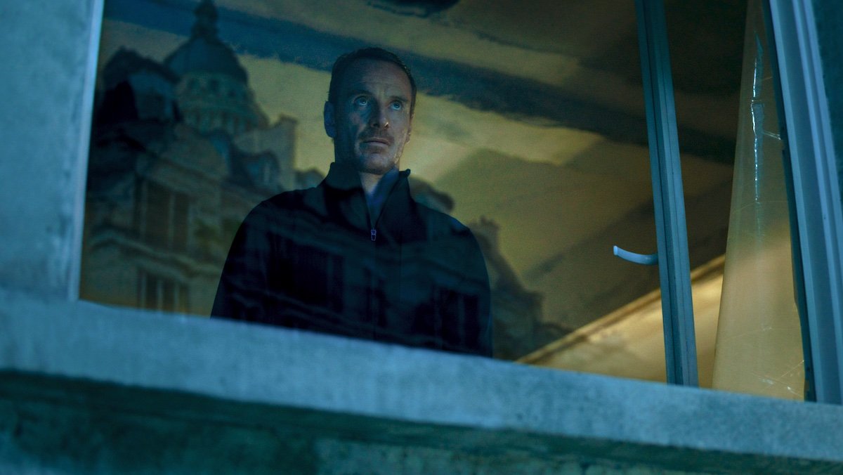 Michael Fassbender looks out a window which reflects a church in The Killer for Netflix ad tier update article