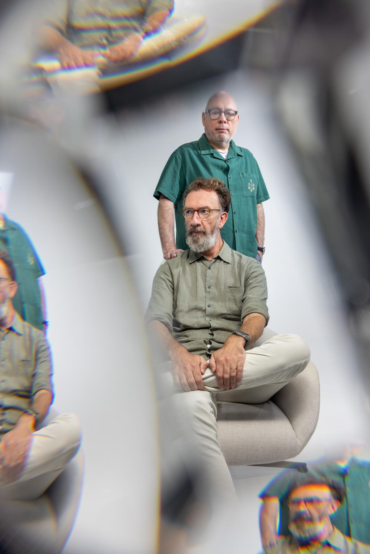 Through a prism: A bearded, bespectacled man in a chair (John Carney) and behind, a bald man in a green shirt (Gary Clark)