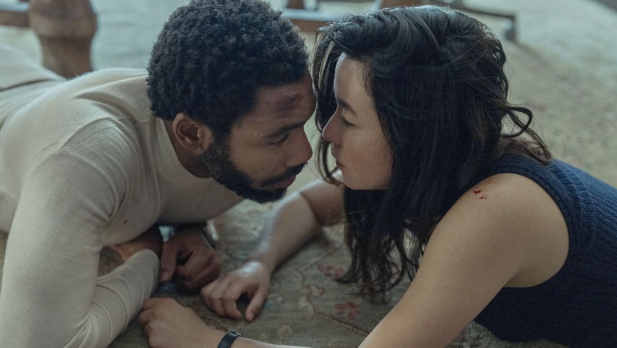 Donald Glover and Maya Erskine lay on a floor and embrace each other on the floor in mr. & mrs. smith trailer