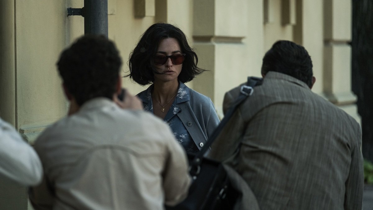 Penelope Cruz with short black hair and sunglasses is photographed by many people in Ferrari