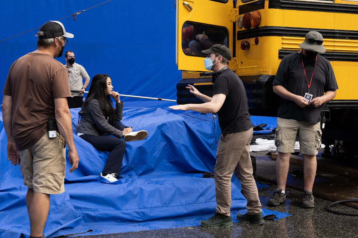 Matt Shakman talking to Anna Sawai on the set of Monarch; she’s sitting on a giant blue screen next to a yellow school bus