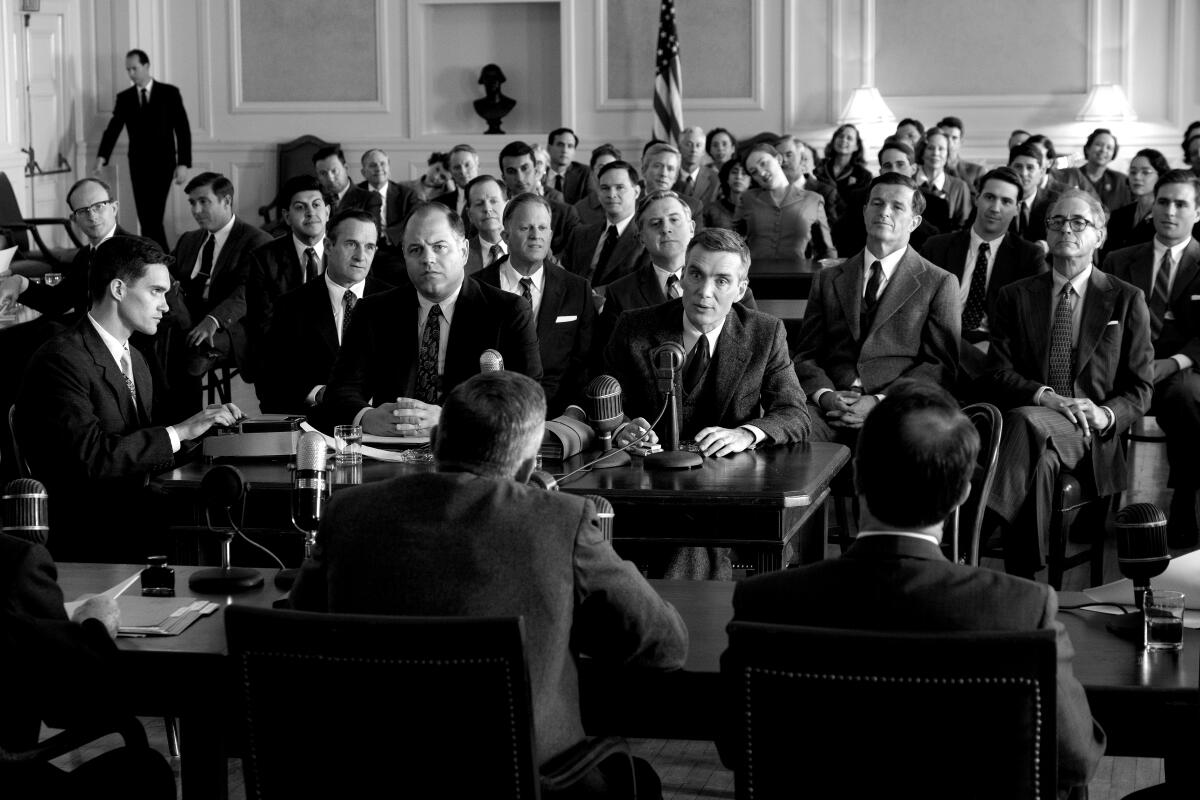 A black and white image of Cillian Murphy in a room full of men in suits in "Oppenheimer."