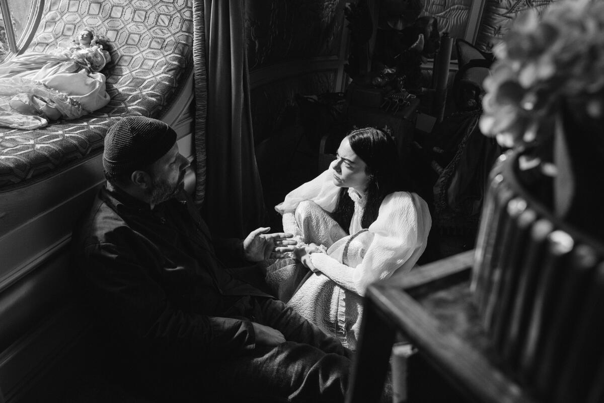 A black and white image of Yorgos Lanthimos and Emma Stone sitting on the floor on the set of "Poor Things."